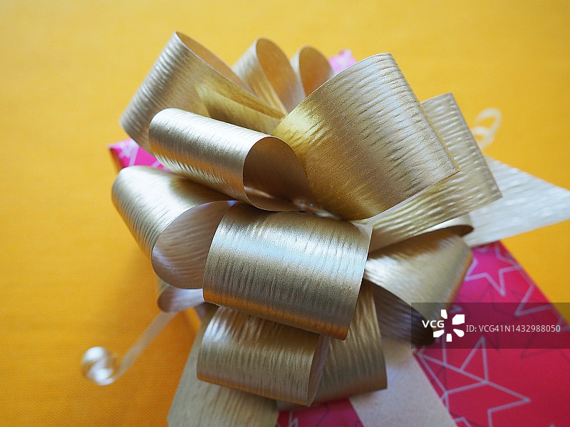 红粉色礼品盒与一个大金色蝴蝶结在黄色赭色的背景。圣诞节，新年，生日，母亲节，婚礼，情人节的礼物。美丽的节日装饰。赠送礼物图片素材