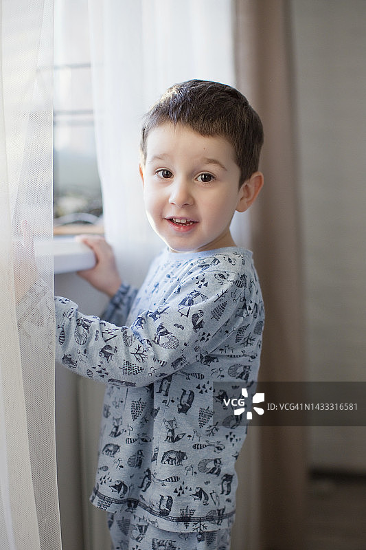 可爱的男孩站在家里的窗户边图片素材