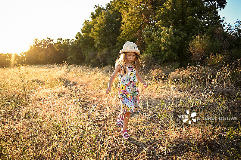 小女孩穿过阳光普照的田野。图片素材