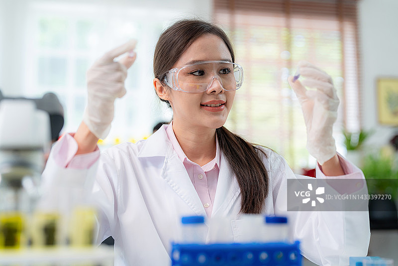 年轻的亚洲研究人员穿着实验服，通过摇晃在epppendorf管中混合溶液。聪明的女人在现代实验室从事医学和生物技术工作。生物植物概念的研究与发展图片素材