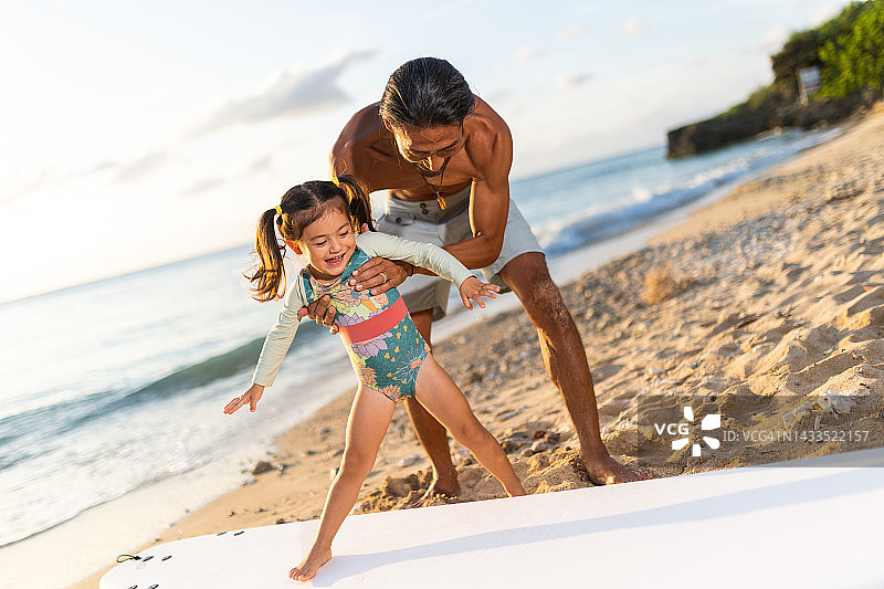 冲浪者的父亲在教他的小女儿如何在海滩上冲浪图片素材