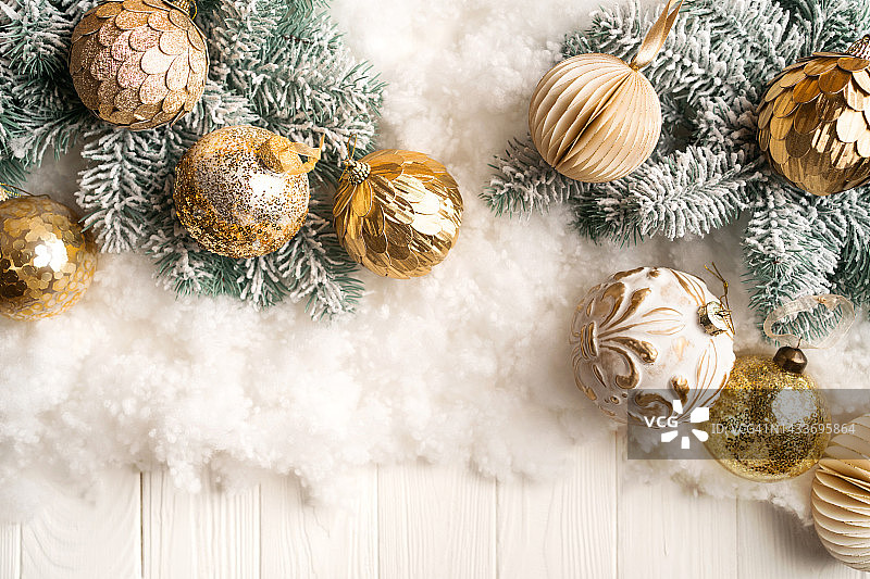 金色的圣诞球在冷杉树的树枝上，在白色的木制背景上的雪。为您设计的新年喜庆背景。从上面拍摄，有复制空间图片素材