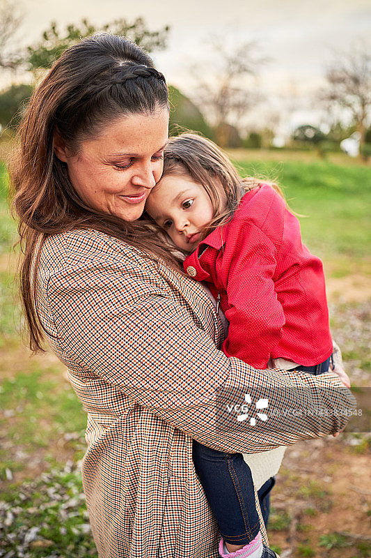 站在户外公园里，一位妇女抱着她的小女儿。图片素材