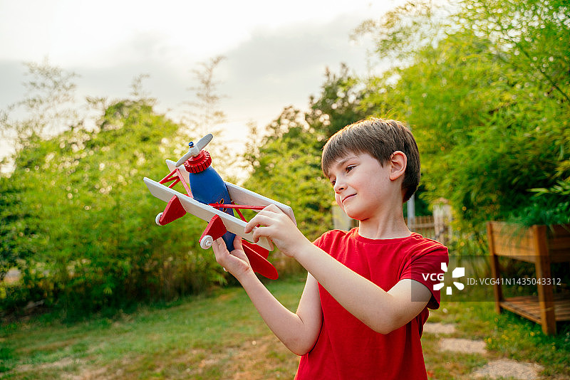 小孩子在绿色的花园背景和红色的衣服上玩手工制作的飞机玩具。图片素材