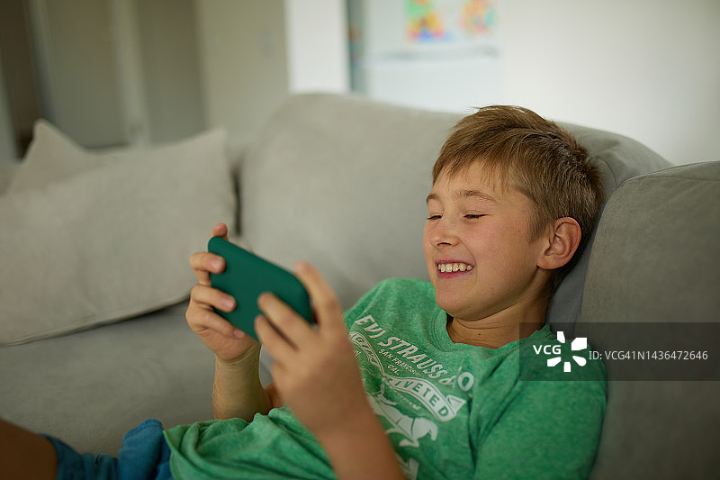 可爱的男孩在家里用智能手机玩电子游戏图片素材