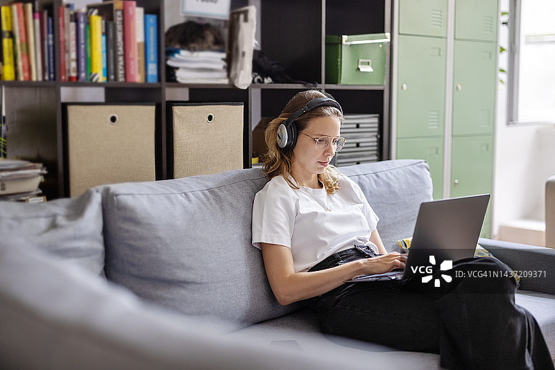 年轻女子戴着耳机在办公室的笔记本电脑前工作图片素材