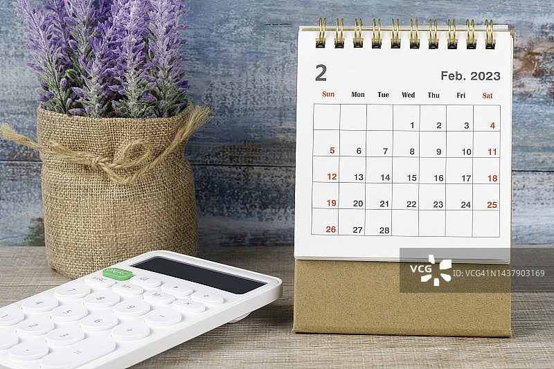 2023日历台:2月是组织者计划和截止日期的月份，白色的计算器在一个古老的木制背景。图片素材
