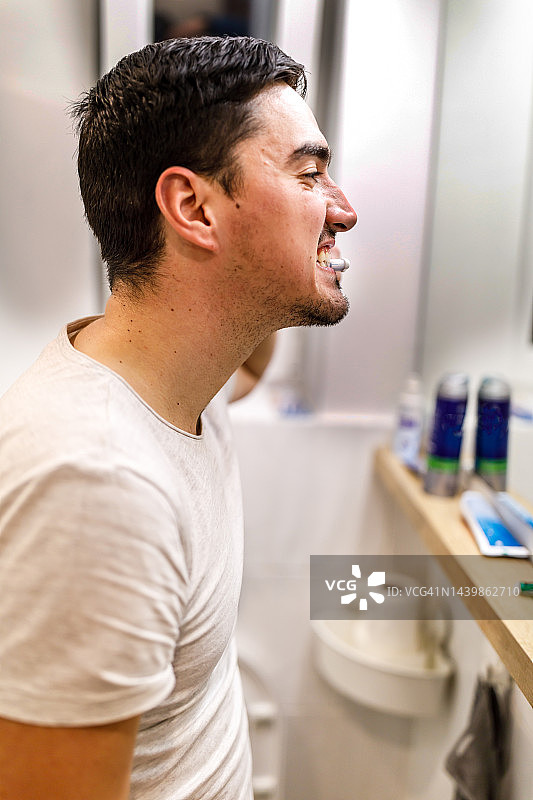 一位英俊的年轻人正站在镜子前刷牙。图片素材