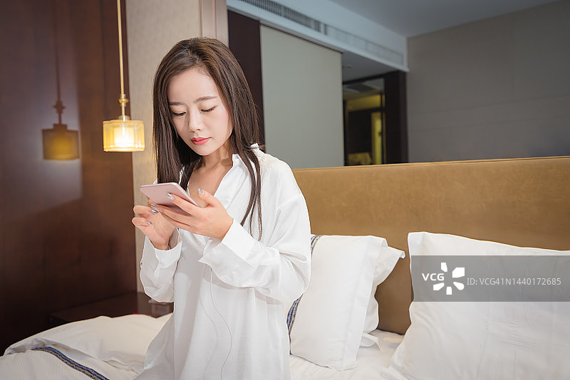 年轻女人坐在床上拿着智能手机图片素材