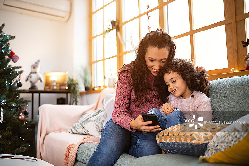 母亲和女儿在视频通话中，在家里享受舒适的圣诞节图片素材