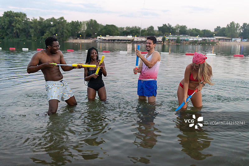 一群多民族的朋友正在河边玩水枪。图片素材