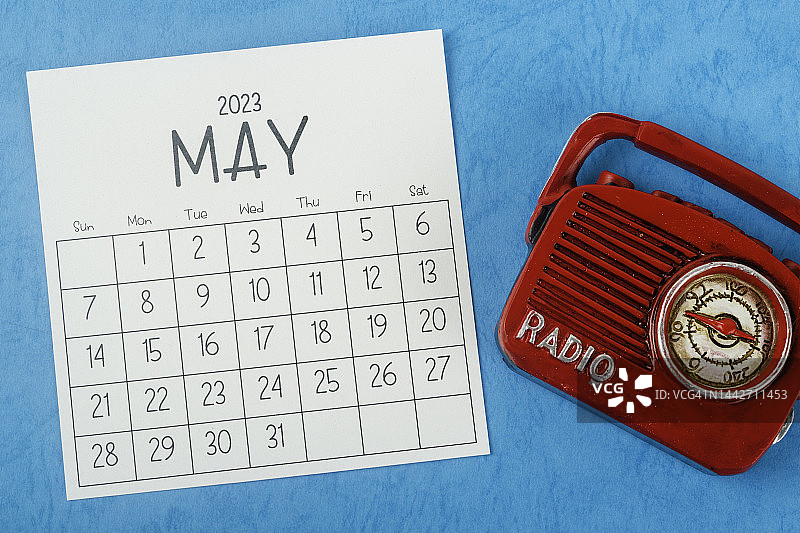 2023日历台:5月是组织者在蓝纸背景下用老式收音机计划和截止日期的月份。图片素材