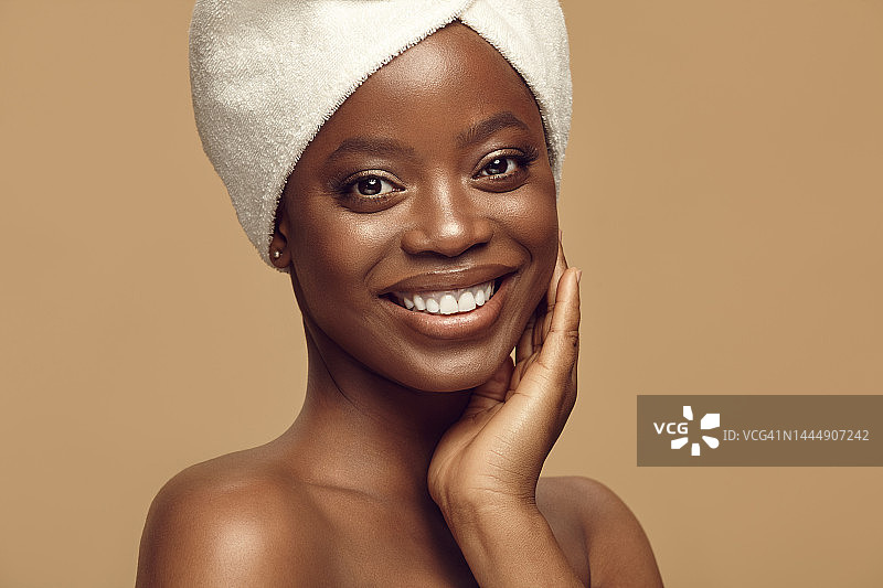 美丽的肖像快乐的非洲裔妇女有健康清洁的皮肤触摸自己的脸和愉快的微笑在米黄色孤立的背景。图片素材