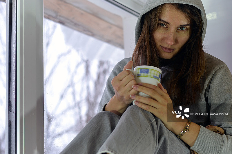 一个年轻女人的画像在窗口喝一杯咖啡。图片素材