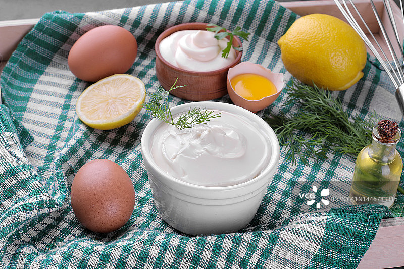 蛋黄酱放在白色的碗里，制作蛋黄酱的材料放在绿色的餐巾上。白汁沙司。图片素材