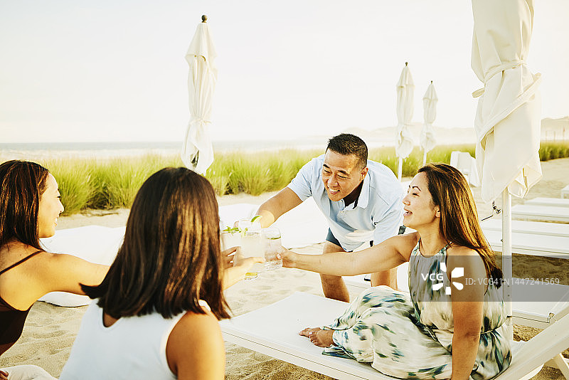 在热带海滩上，微笑的家人举杯祝酒的中景图片素材