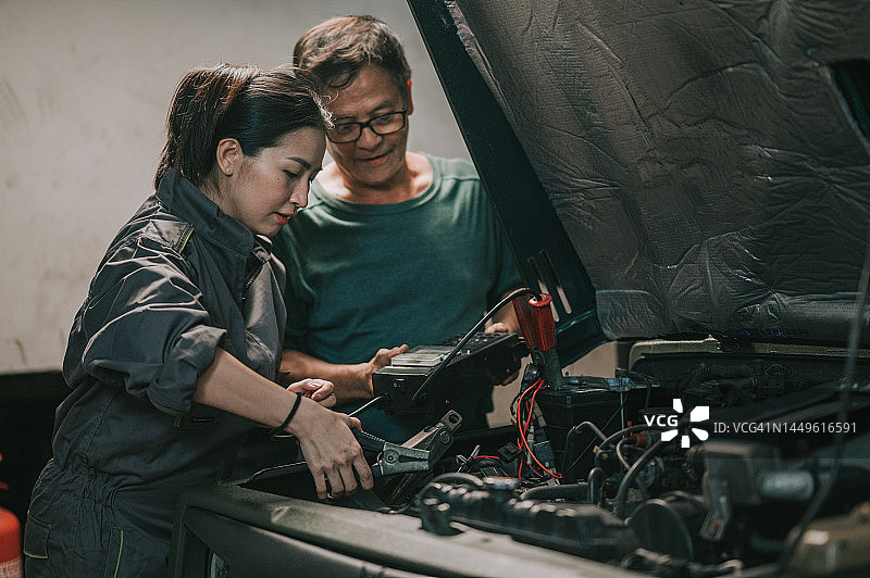 资深亚裔华人机械师指导学员检查汽车修理厂电池电量图片素材