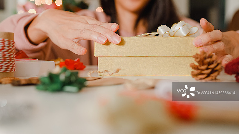 特写的妇女手包装圣诞礼物盒在家里的桌子上。图片素材