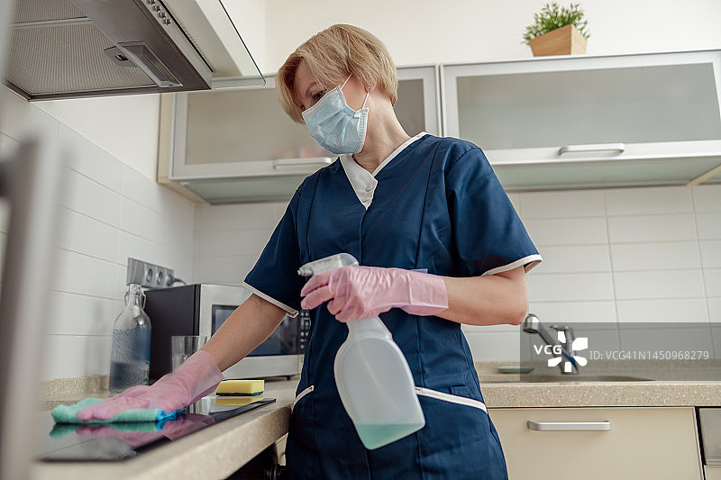 戴着防护手套的女佣在厨房用抹布和有效的洗涤剂清洁工作台面图片素材
