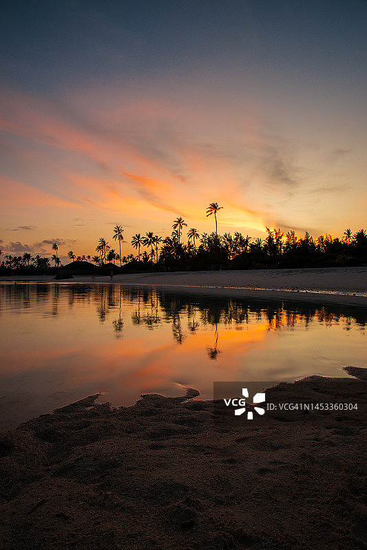 五彩缤纷的日落在海滩与水反射热带马尔代夫岛的棕榈树图片素材