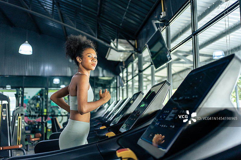 非裔美国年轻女运动员在健身房的跑步机上跑步锻炼。有吸引力的美丽的运动员女孩练习锻炼，以保持肌肉和燃烧卡路里的健康福利在健身场馆图片素材