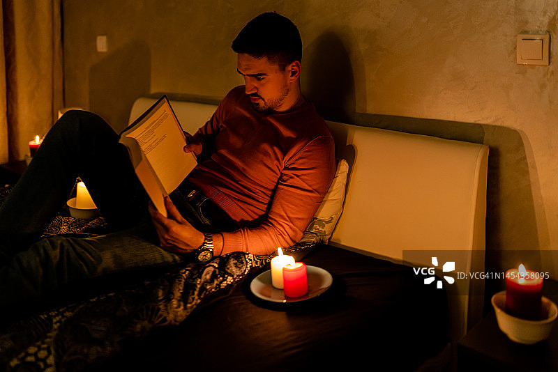一个年轻人在家里遭遇电力危机，正在看书。图片素材