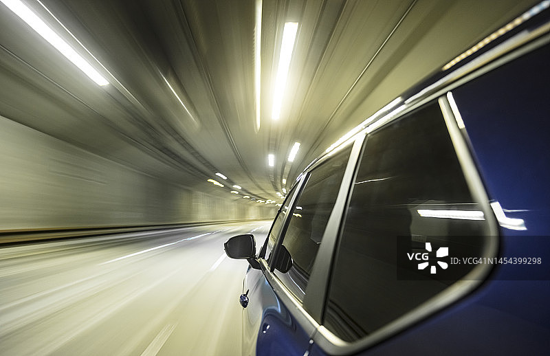 蓝色混合动力汽车在高速公路上快速驶入照明的未来公路隧道。图片素材