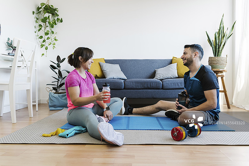 一对夫妇在锻炼后坐在家里的客厅里拿着水合瓶聊天图片素材