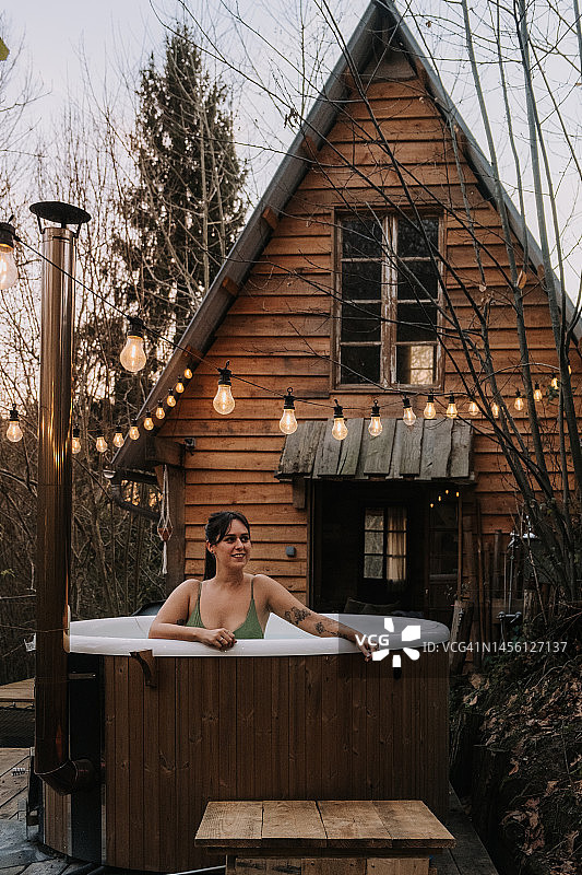 一个成年女子躺在木屋旁的北欧浴缸里图片素材