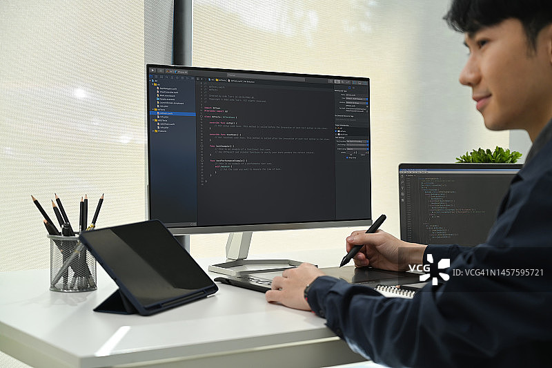 男程序员在笔记本电脑上工作的侧面视图，检查IT办公室漏洞系统中的编码。图片素材