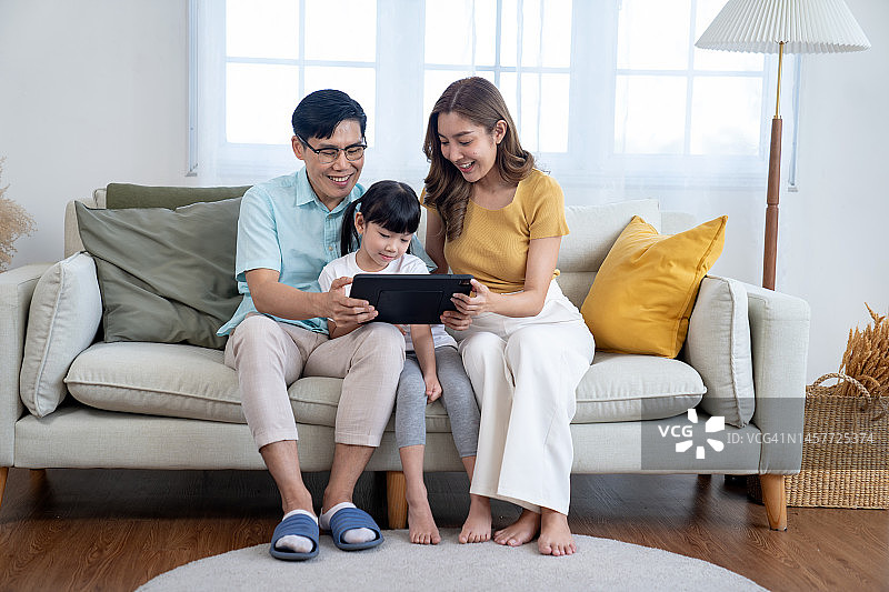 亚洲家庭在家里快乐地使用平板电脑图片素材