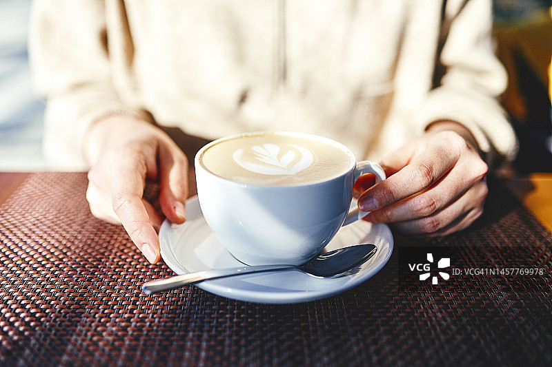 街道上一家咖啡店里，一位身份不明的女士在阳光下端着一杯咖啡，图片素材