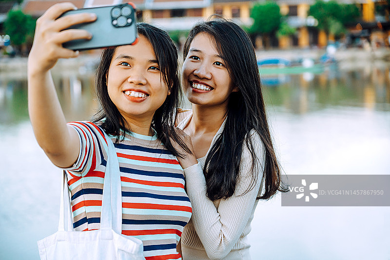 两名年轻的亚洲女子在越南会安的河边散步道自拍图片素材