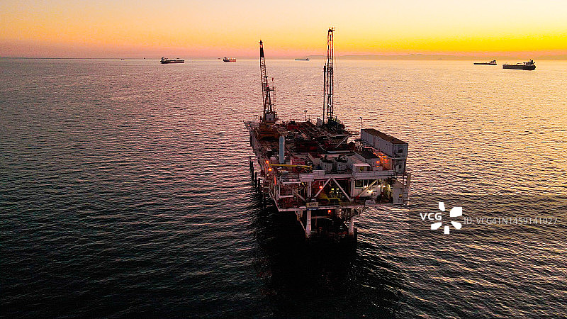 无人机查看大型工业天然气和石油海上钻井平台在平静的海面上，在一个晴朗的傍晚，远处的背景是卡特琳娜岛图片素材