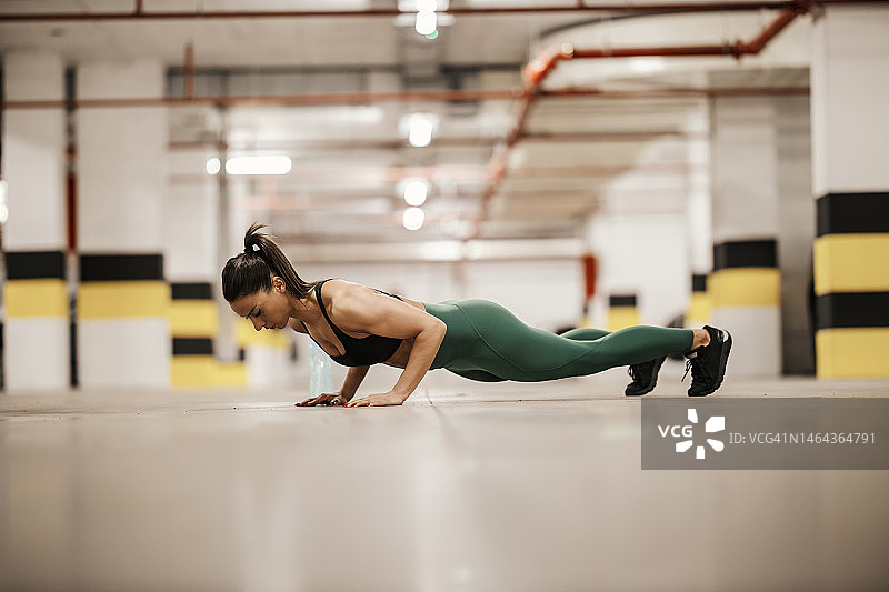 一个城市肌肉女运动员正在地下车库做俯卧撑。图片素材