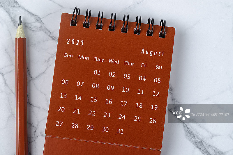 2023年日历桌面的俯视图:7月是组织者用红色铅笔在白色大理石背景上制定计划和截止日期的月份。图片素材