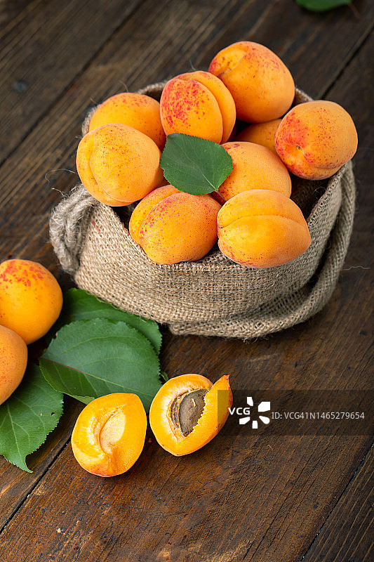 熟杏和杏叶装在一个袋子里，放在木桌上。图片素材