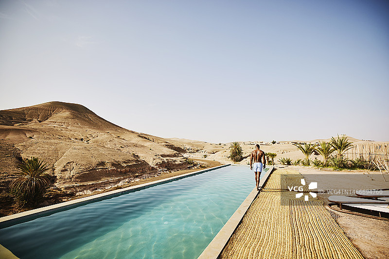 宽阔的镜头，男子在摩洛哥沙漠营地的游泳池边散步图片素材