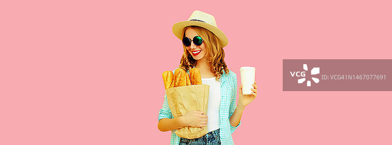 微笑的年轻女子手持杂货店购物纸袋长白面包法棍和咖啡杯在粉红色的背景图片素材