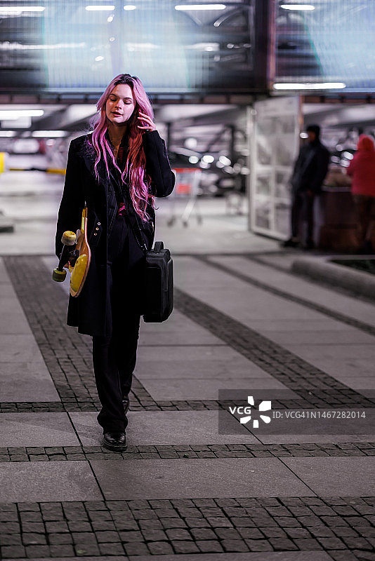 一位美女在城市里踩着滑板，边走边打电话。图片素材