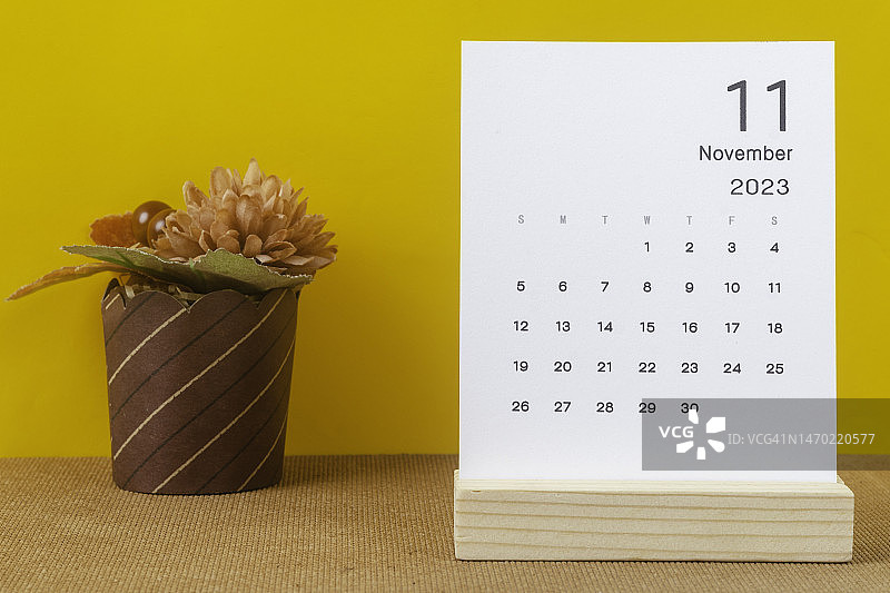 2023日历台:11月是组织者计划和截止日期的月份，在黄色纸背景上手工制作一朵花。图片素材