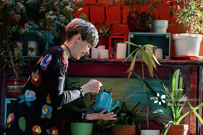 成年快乐的女人穿着复古针织外套浇盆花在舒适的庭院区域图片素材
