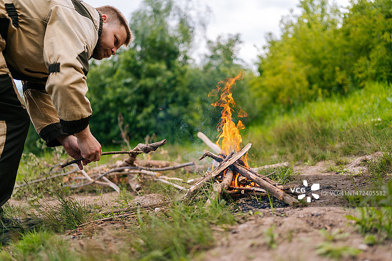 低角度视角，熟练的渔夫在日落前做饭前，在河岸上把柴火放在营火上生火。图片素材