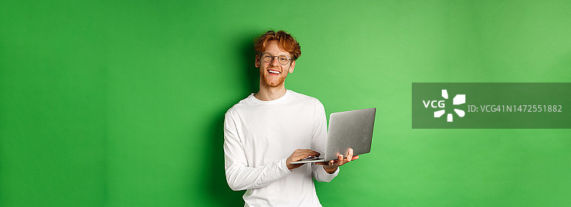 开朗的红头发自由职业者，戴着眼镜，对着镜头微笑，继续工作图片素材