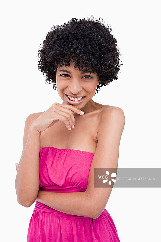 年轻的微笑女人站在她的双臂交叉，她的手放在下巴图片素材