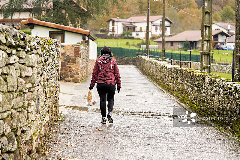 一个女人在阴冷的日子里走过一条小路的后视图。一个女人雨后走过一条小路。图片素材