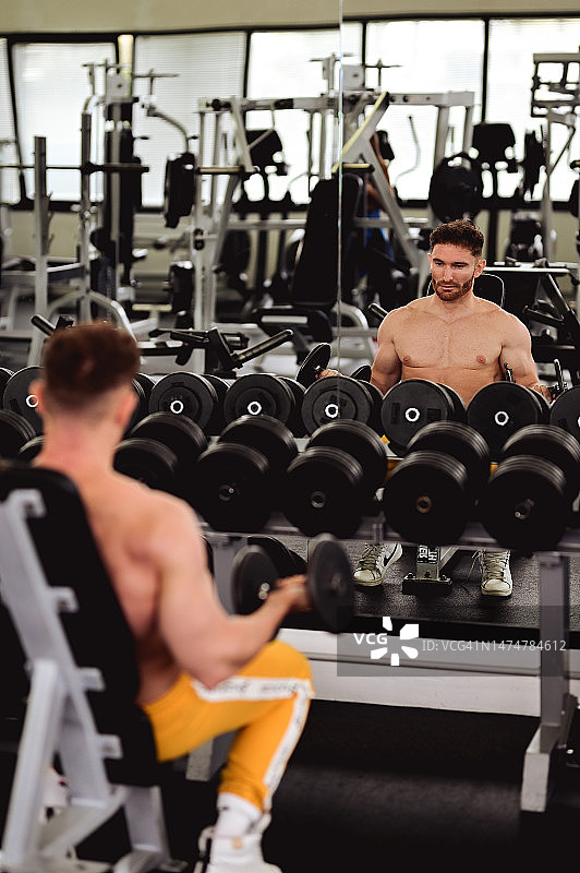 一个男人在健身房锻炼的肖像，看着镜子。图片素材