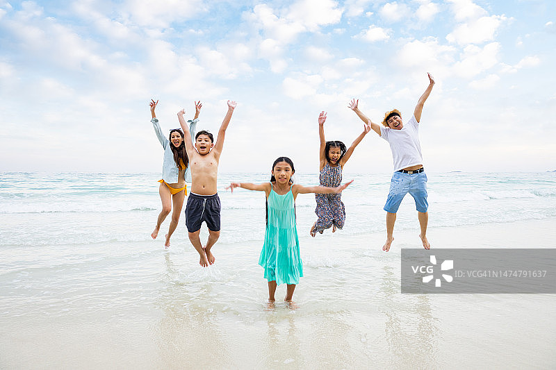 快乐的亚洲家庭一起在海滩上跳在假期。幸福家庭旅游度假理念。图片素材