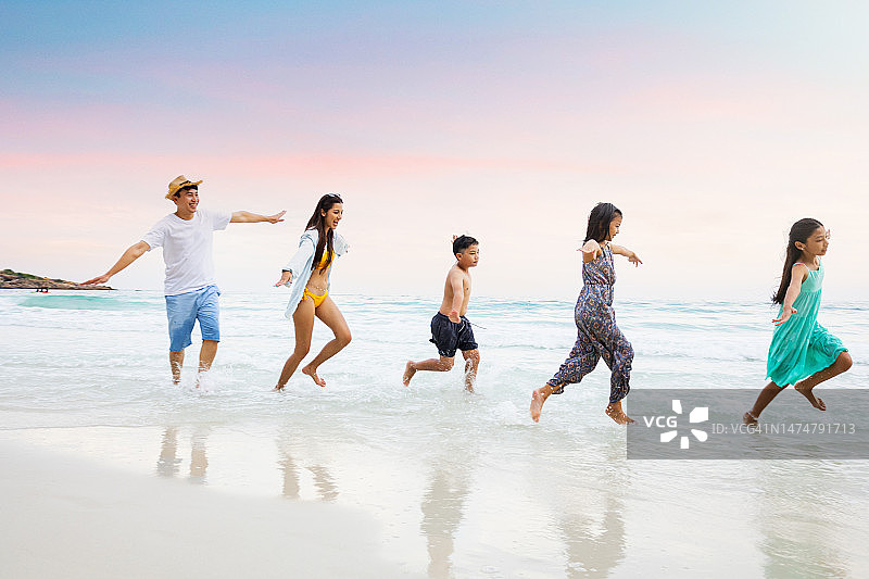 在一次假期中，一位家长和三个孩子在海滩上蹦蹦跳跳。图片素材