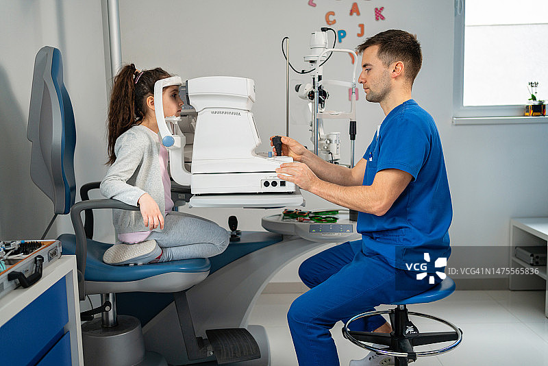 男性眼科医生用自动折射镜检查小女孩的眼睛，在诊所图片素材